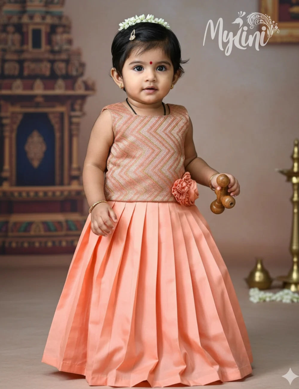 Young girl in a peach dress with floral details, holding toys, in a decorated room.